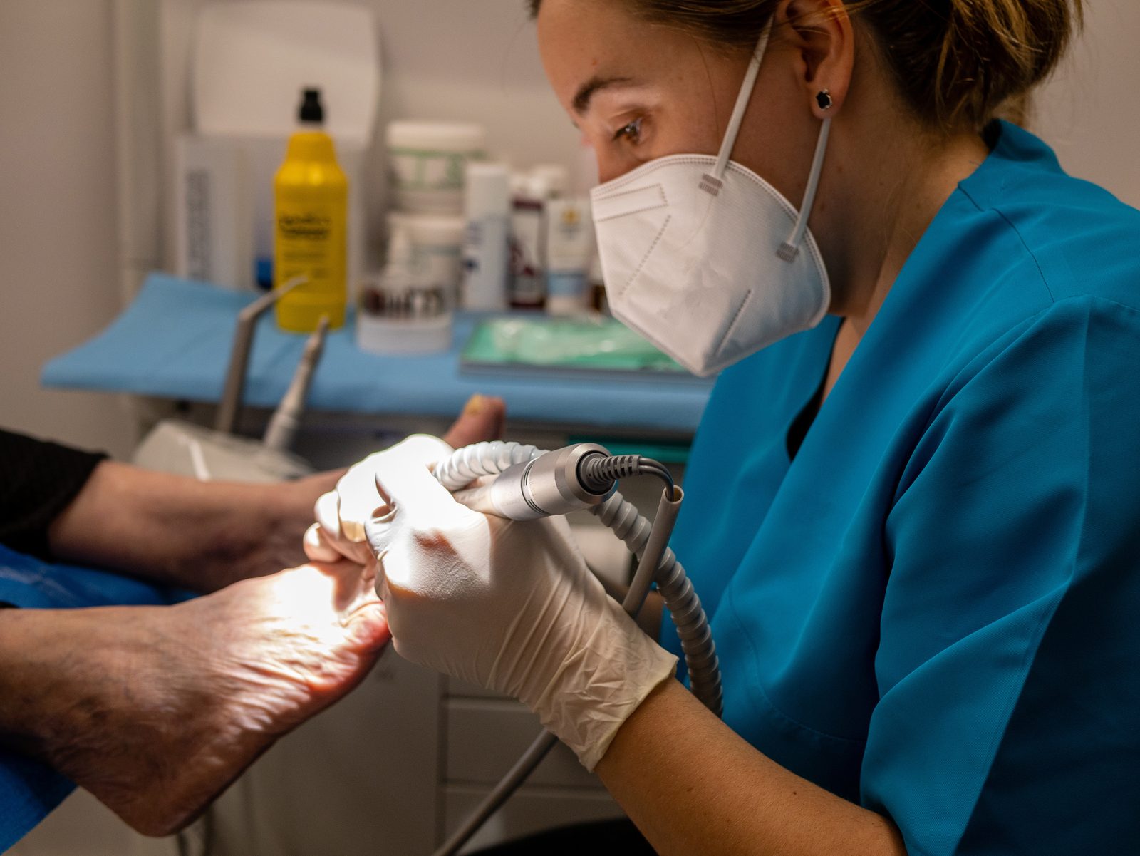 Podóloga certificada con guantes y mascarilla atendiendo los pies de una paciente